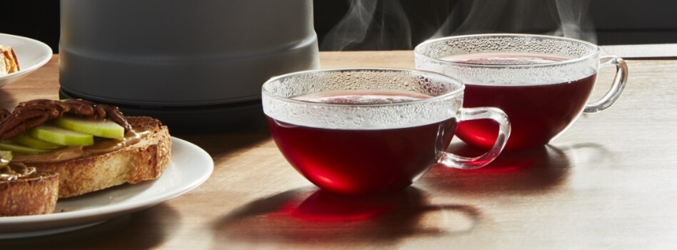 Two cups of tea in front of a KitchenAid Kettle. Next to them is a plate of toast. 